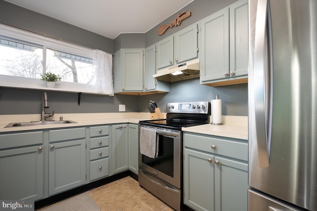 kitchen featuring appliances with stainless steel finishes, a sink, light countertops, under cabinet range hood, and gray cabinetry