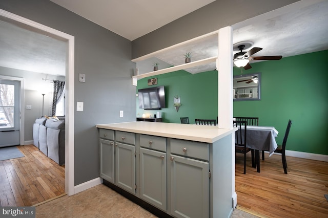 kitchen with light wood-style floors, light countertops, gray cabinets, a ceiling fan, and a peninsula