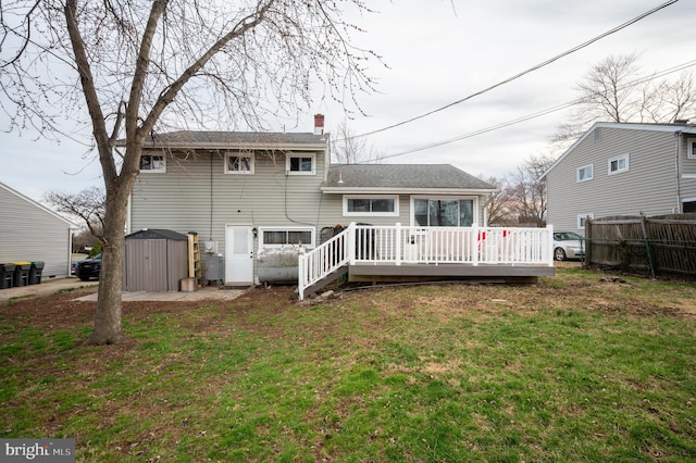 back of house featuring a deck, a shed, a chimney, a lawn, and an outbuilding