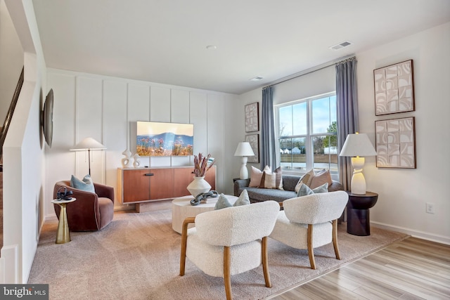 living room featuring visible vents, baseboards, a decorative wall, and wood finished floors