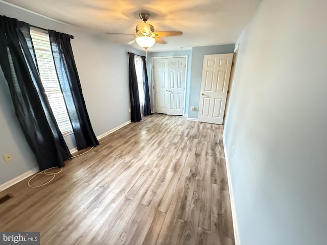 unfurnished bedroom featuring baseboards, light wood finished floors, ceiling fan, and a closet