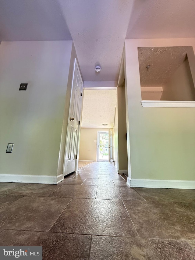 hall with stone tile flooring, baseboards, and a textured ceiling