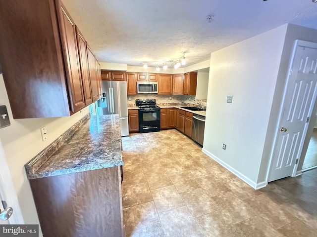 kitchen with a textured ceiling, brown cabinets, a sink, appliances with stainless steel finishes, and backsplash