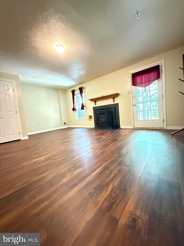 unfurnished living room with a textured ceiling, baseboards, wood finished floors, and a fireplace