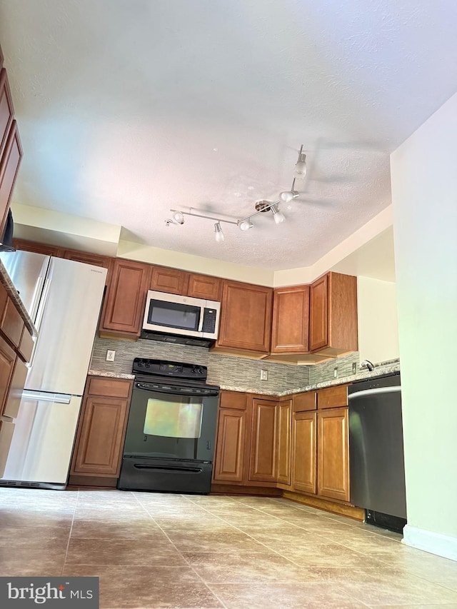 kitchen with dishwasher, brown cabinetry, black electric range oven, freestanding refrigerator, and stainless steel microwave