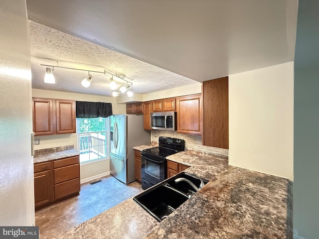 kitchen with a textured ceiling, tasteful backsplash, brown cabinets, a sink, and stainless steel appliances