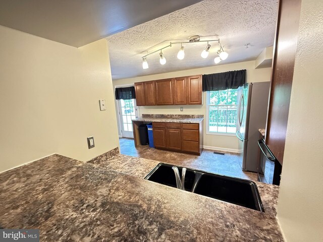 kitchen featuring dark countertops, freestanding refrigerator, brown cabinets, and a textured ceiling