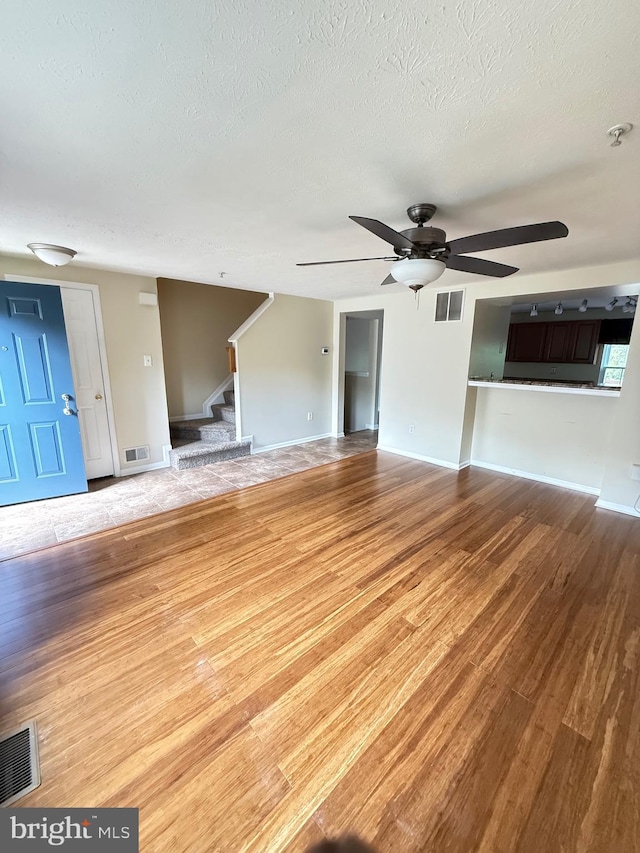 unfurnished living room featuring visible vents, stairs, ceiling fan, and wood finished floors