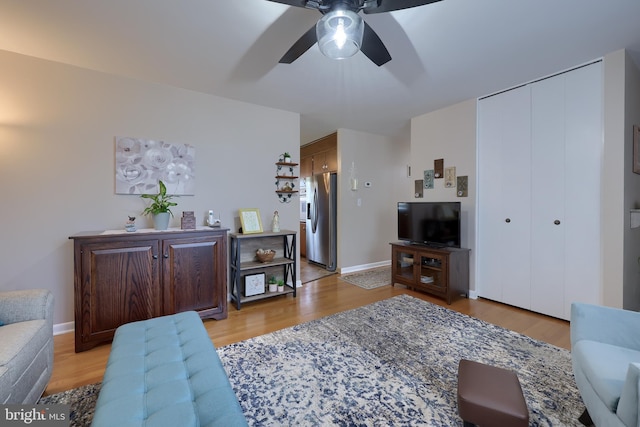 living area featuring a ceiling fan, baseboards, and light wood-style flooring