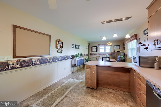 kitchen featuring wainscoting, light countertops, a peninsula, stainless steel dishwasher, and pendant lighting