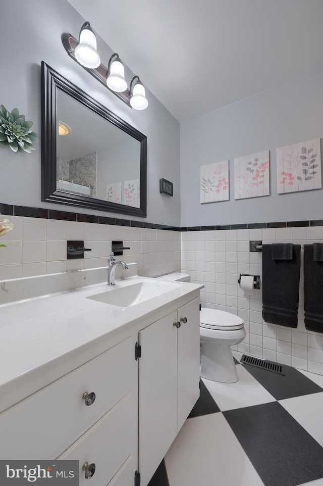 bathroom featuring wainscoting, vanity, toilet, tile walls, and visible vents
