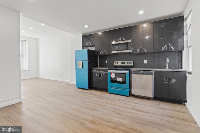 kitchen featuring light wood finished floors, dark cabinetry, stainless steel appliances, baseboards, and decorative backsplash