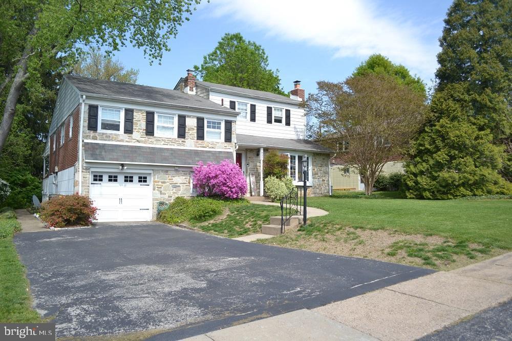 view of front of property featuring driveway, a chimney, a front lawn, an attached garage, and stone siding
