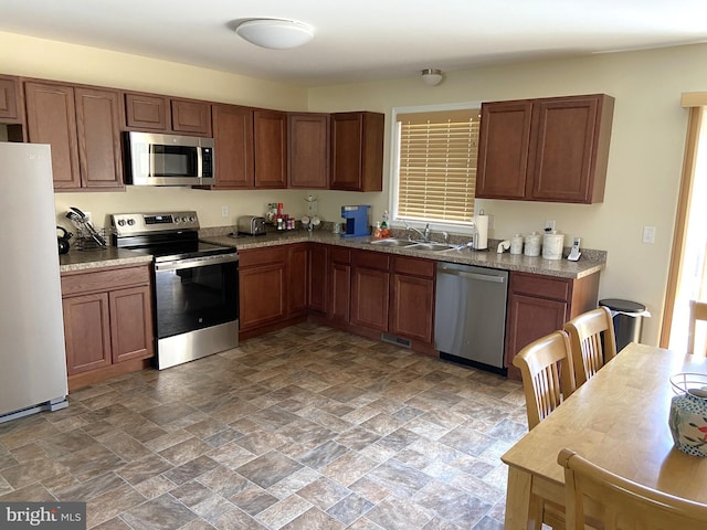 kitchen with stone finish floor, visible vents, brown cabinets, a sink, and stainless steel appliances
