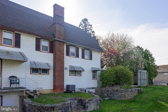 104 N Custer Ave, New Holland, PA 17557 - back of property featuring a shingled roof, central air condition unit, a chimney, and a lawn