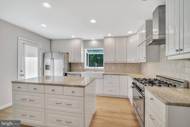 kitchen with a sink, light wood finished floors, wall chimney exhaust hood, stainless steel appliances, and tasteful backsplash