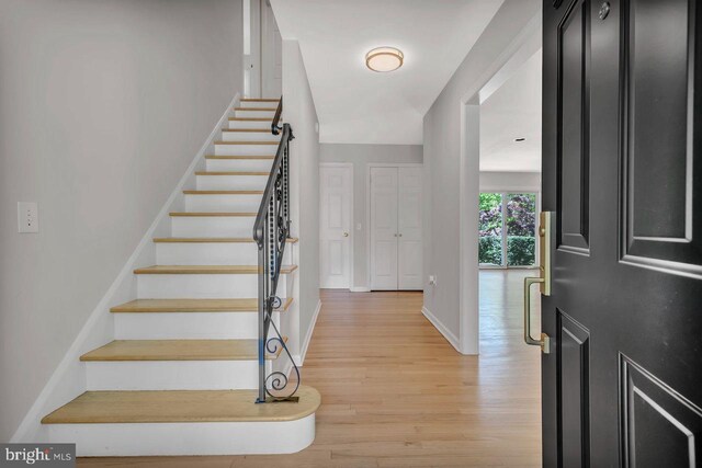 foyer entrance with baseboards, light wood finished floors, and stairs