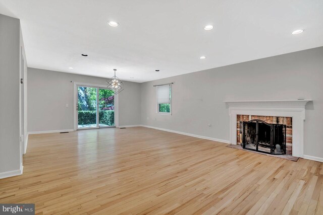 unfurnished living room featuring light wood-style floors, baseboards, a brick fireplace, and a chandelier