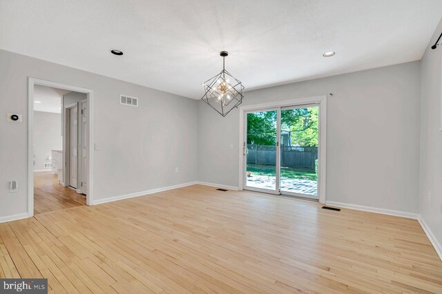unfurnished room with an inviting chandelier, baseboards, light wood finished floors, and visible vents