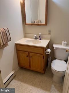 half bath featuring vanity, tile patterned flooring, baseboard heating, and toilet