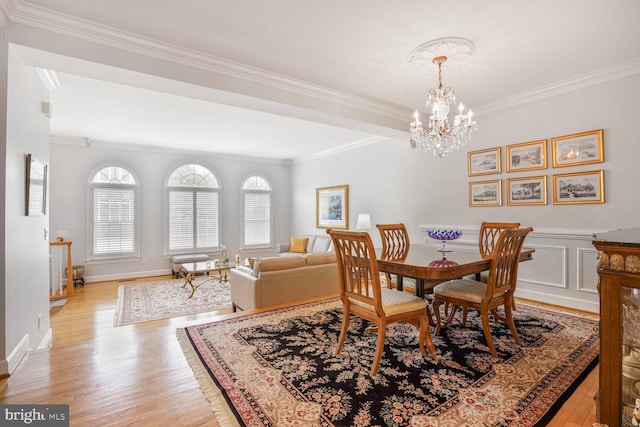 dining room with light wood-type flooring, baseboards, ornamental molding, and a notable chandelier