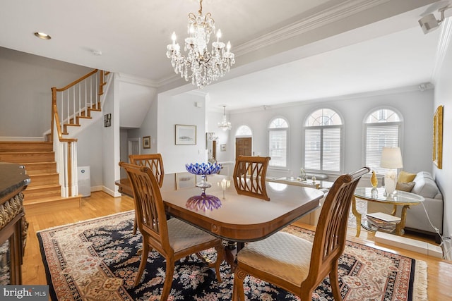 dining room with light wood finished floors, crown molding, a chandelier, and stairs