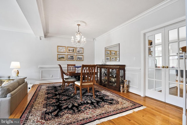 dining space with french doors, wood finished floors, a notable chandelier, crown molding, and wainscoting
