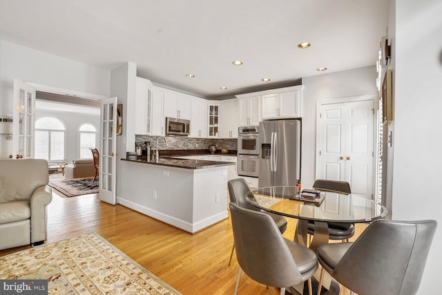 kitchen with light wood-style flooring, glass insert cabinets, white cabinetry, a peninsula, and appliances with stainless steel finishes