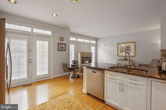 kitchen with a sink, dark stone countertops, visible vents, a glass covered fireplace, and appliances with stainless steel finishes