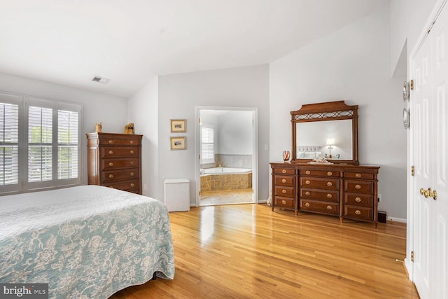 bedroom with light wood-style floors, visible vents, baseboards, ensuite bath, and lofted ceiling
