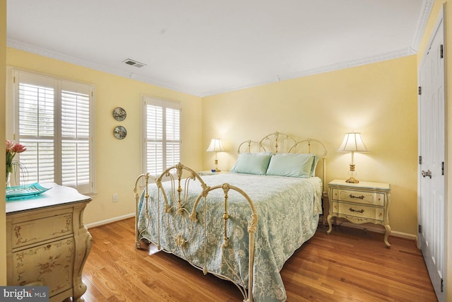 bedroom featuring crown molding, visible vents, wood finished floors, and baseboards