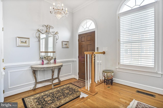 entryway featuring visible vents, wood finished floors, ornamental molding, and a notable chandelier