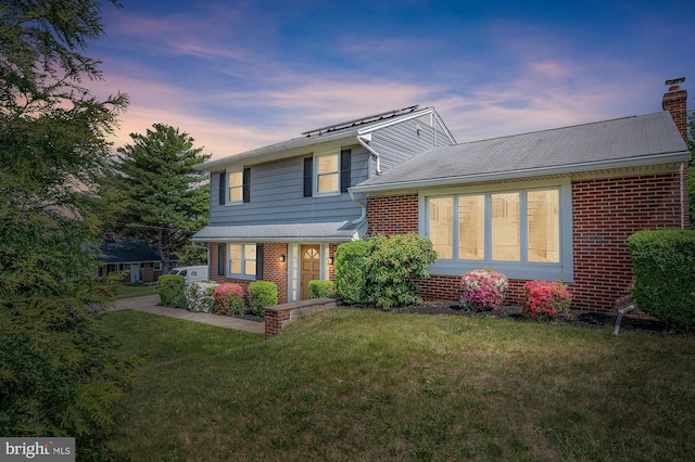 tri-level home with a yard, brick siding, and a chimney