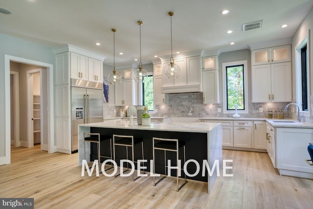 kitchen with a breakfast bar area, visible vents, stainless steel built in fridge, a center island, and a sink