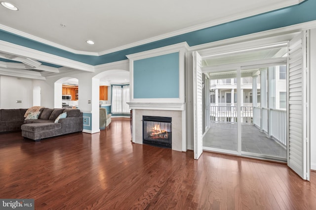 living room with a tiled fireplace, arched walkways, dark wood-style floors, ornamental molding, and recessed lighting