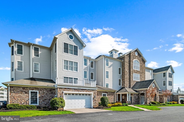 multi unit property with a garage, driveway, a front lawn, and stone siding