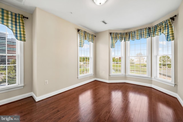 unfurnished room with baseboards, wood finished floors, a wealth of natural light, and visible vents