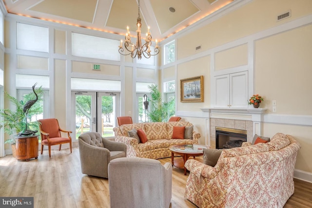 living room with a high ceiling, a notable chandelier, light wood-style floors, a tile fireplace, and visible vents