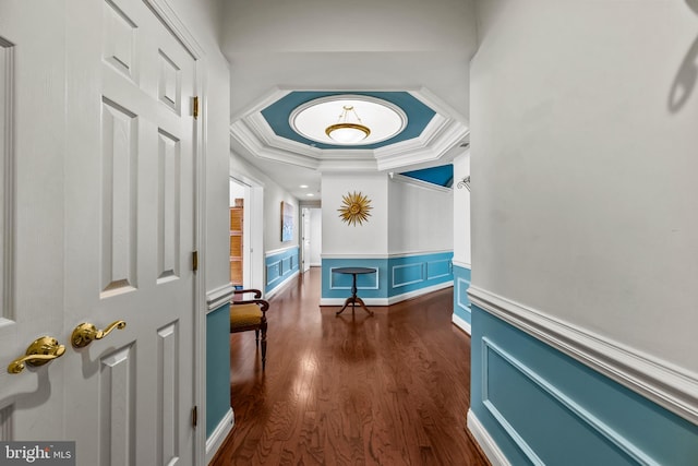 hallway featuring crown molding, dark wood-style flooring, a tray ceiling, and wainscoting