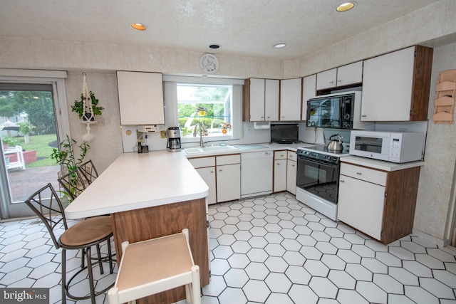 kitchen featuring white appliances, a sink, a peninsula, healthy amount of natural light, and recessed lighting