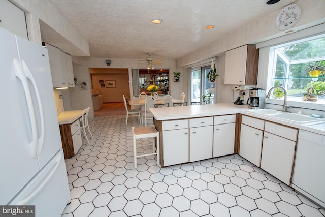 kitchen with white appliances, a sink, ceiling fan, light countertops, and a peninsula