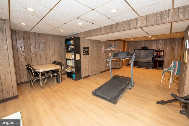 exercise room with a paneled ceiling, wooden walls, wood finished floors, and recessed lighting
