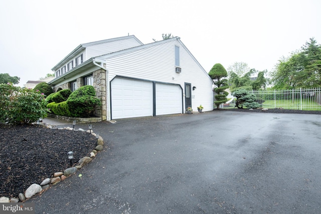 view of side of property with fence, stone siding, driveway, and an attached garage