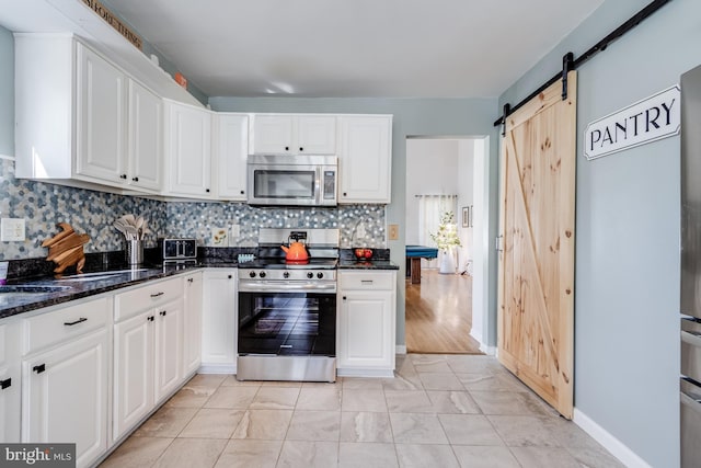 kitchen featuring appliances with stainless steel finishes, a barn door, dark stone countertops, white cabinetry, and tasteful backsplash