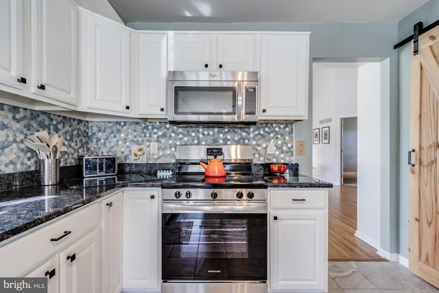 kitchen featuring tasteful backsplash, stainless steel appliances, a barn door, and white cabinetry