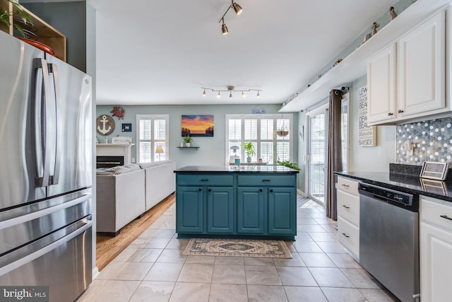 kitchen with white cabinets, appliances with stainless steel finishes, a fireplace, open floor plan, and blue cabinets