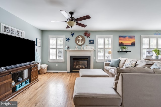living area with ceiling fan, a glass covered fireplace, a wealth of natural light, and wood finished floors