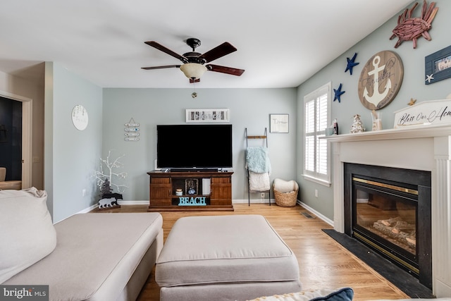 living room with a ceiling fan, baseboards, a fireplace with flush hearth, and wood finished floors