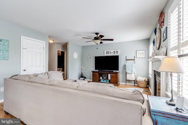 living area with a glass covered fireplace, a ceiling fan, wood finished floors, and a wealth of natural light