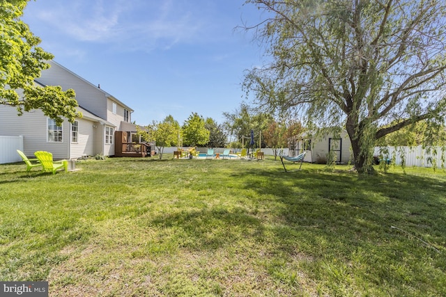 view of yard with fence, a wooden deck, a shed, a fenced in pool, and an outdoor structure